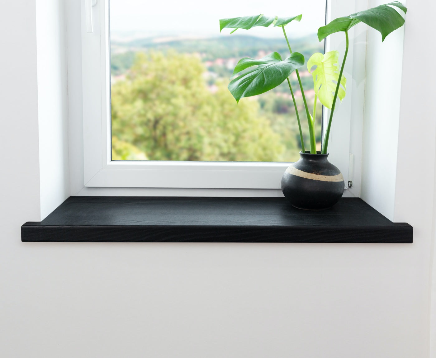 Schwarze Aufsatzfensterbank aus Holz im Innenbereich, mit Topfpflanze. Verdeckt alte Fensterbank.