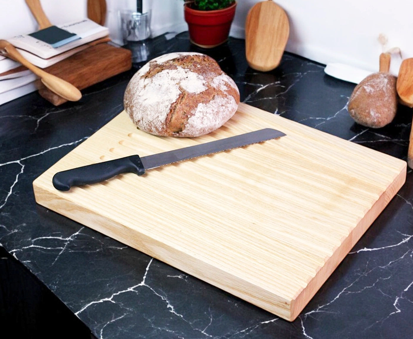 Brotschneidebrett mit Rillen aus Esche, mit Messer und Brotlaib auf Küchenzeile.