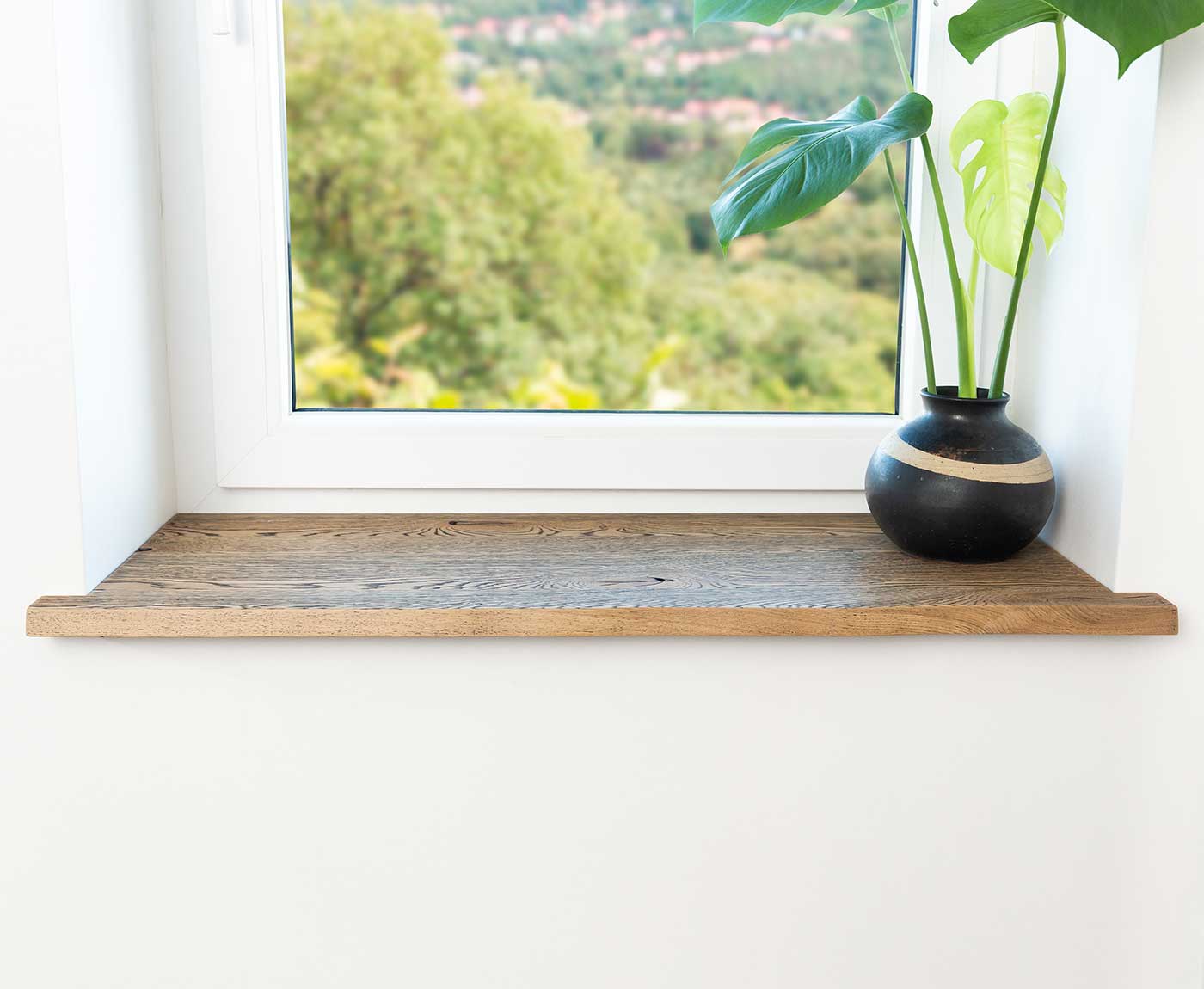 Frontaler Blick auf Fensterbank Altholz mit schwarzer Vase und Pflanze. 