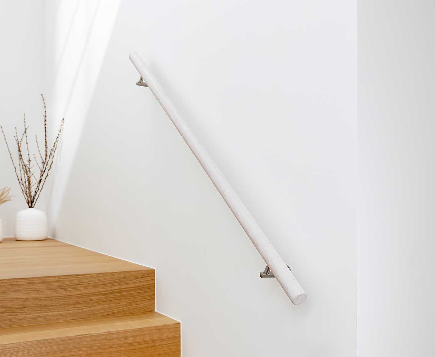 Weißer, runder Handlauf, als Treppengeländer an weißer Wand montiert.