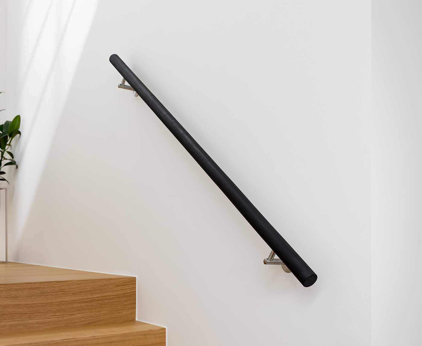 Schwarzer, runder Handlauf Holz, als Treppengeländer an weißer Wand montiert.