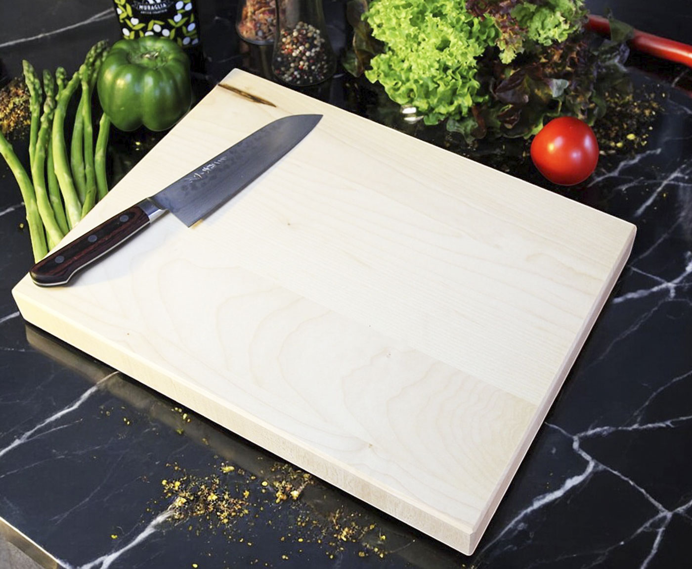 Helles Küchenbrett Holz aus Ahorn mit Messer und Gemüse auf schwarzer Arbeitsplatte.