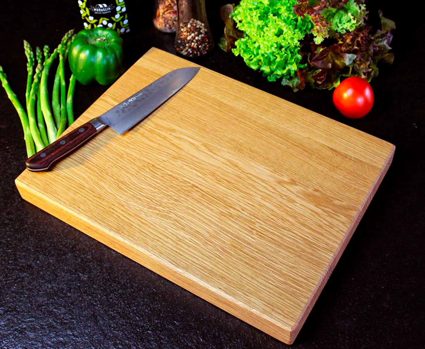 Küchenbrett Holz, Schneidebrett aus Eiche auf schwarzer Arbeitsplatte mit Gemüse und Messer dekoriert.