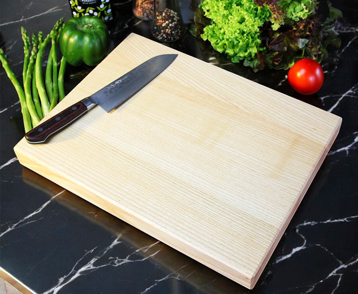 Küchenbrett, Schneidebrett aus Esche, mit Messer und Gemüse im Hintergrund.